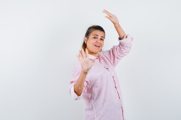 Portrait of young female posing with raised hands in pink shirt and looking charming front view