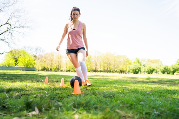 Free photo portrait of young female soccer player running around cones while practicing with ball on field