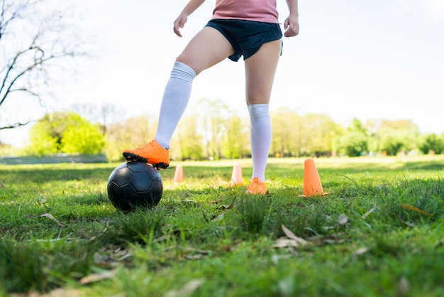 Portrait of young female soccer player running around cones while practicing with ball on field