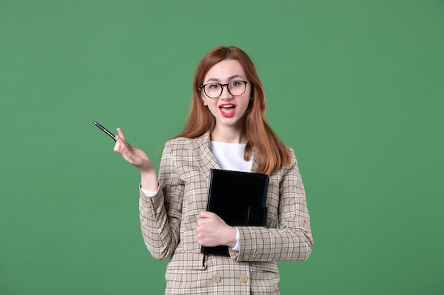 Free photo portrait of young female teacher in suit with notepad on green