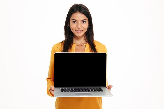 Portrait of young friendly woman showing blank screen laptop computer