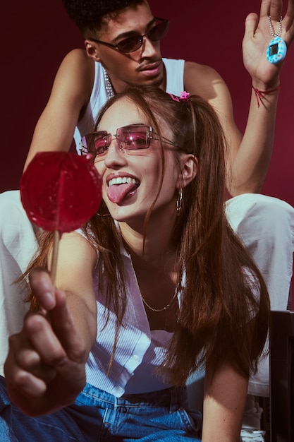 Portrait of young friends in 2000s fashion style posing with lollipop and game