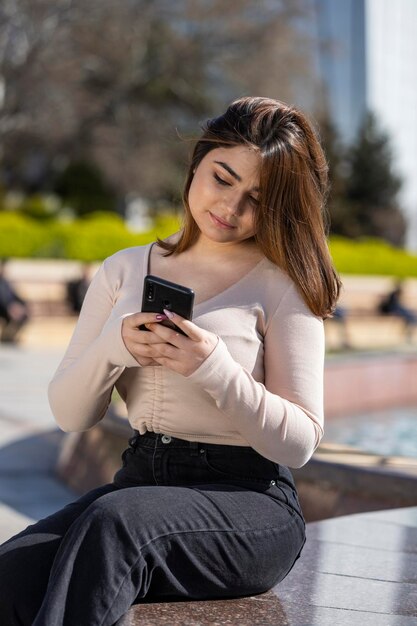 Portrait of young girl holding phone and sitting at the park High quality photo