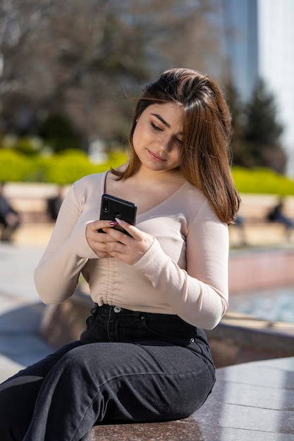 Portrait of young girl holding phone and sitting at the park High quality photo