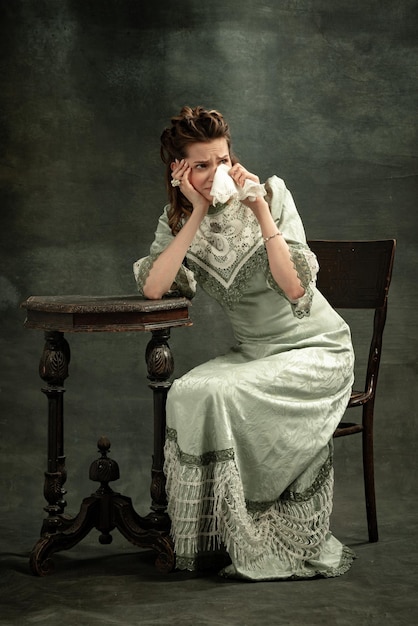 Portrait of young girl in image of medieval royal person in renaissance style dress drinking coffee isolated on dark background