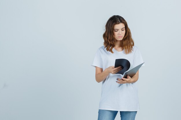 Portrait of young girl looking over notes in folder in white t-shirt and looking focused front view