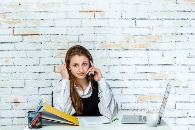 Portrait of young girl sitting behind her desk and and talking on the phone