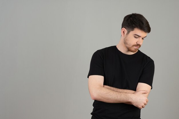 Portrait of young guy. Handsome guy crossed his arms on a grey.