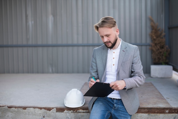 Free photo portrait of young handsome architect writing on clipboard at outdoors