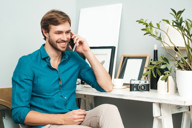 Free Photo portrait of young handsome business man. thoughtful male dressed in blue jeans shirt. bearded model posing at office near paper desk and speaking on the phone.