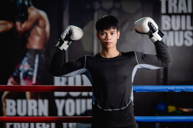 Portrait young handsome man in sportswear and white boxing gloves standing raise arms up to pose on canvas in fitness gym, Healthy man workout boxing class,, 