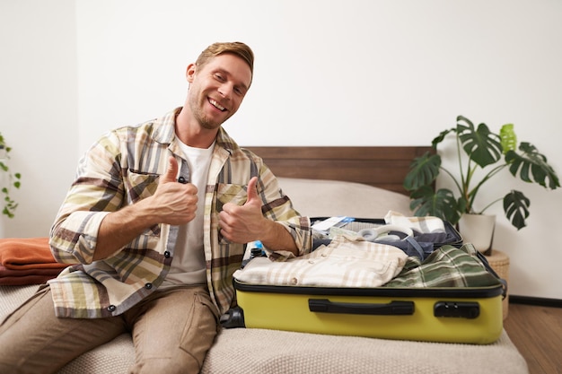 Free photo portrait of young handsome man tourist going on vacation packing luggage for holidays putting