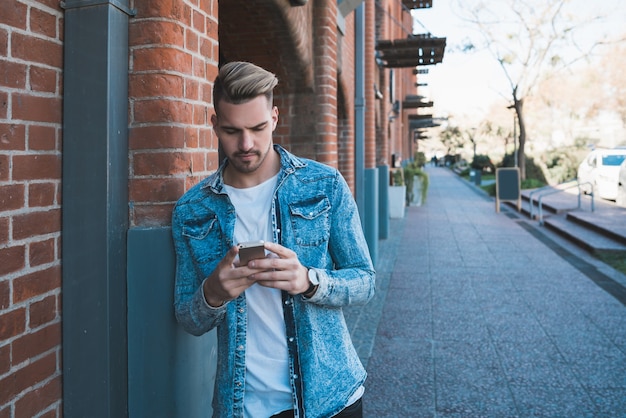 Portrait of young handsome man using his mobile phone outdoors in the street. Communication concept.