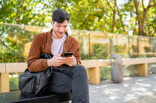 Portrait of young handsome man using his mobile phone while sitting outdoors. Communication and urban concept.