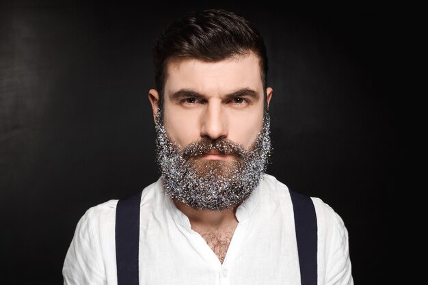 Portrait of young handsome man with beard in snow over black.