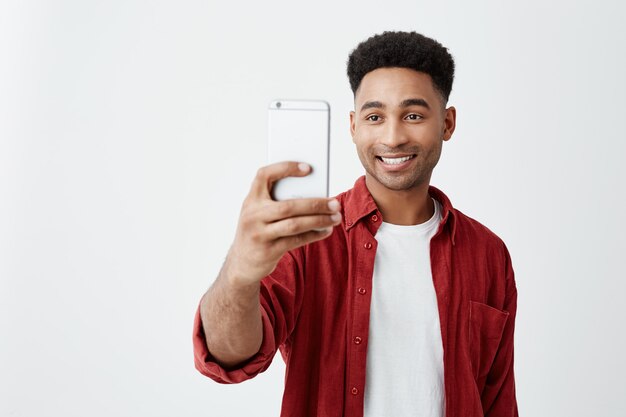 Portrait of young handsome tan-skinned american male with afro hairstyle in casual fashionable outfit smiling with teeth, taking photo of friends during vacation.