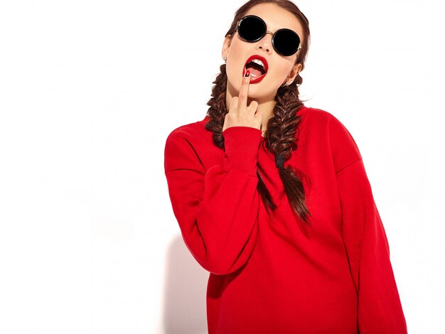 Portrait of young happy smiling woman model with bright makeup and colorful lips with two pigtails and sunglasses in summer red clothes isolated. Licking middle finger, fuck off sign