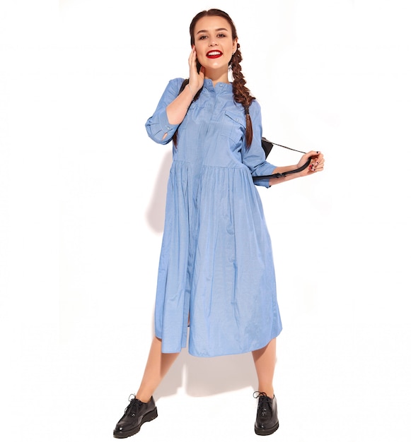 Free photo portrait of young happy smiling woman model with bright makeup and red lips with two pigtails in hands in summer colorful blue dress and backpack isolated.