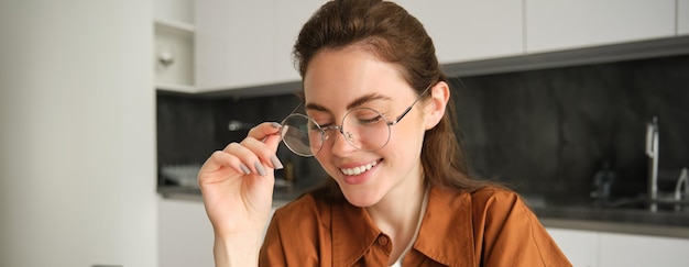 Free Photo portrait of young happy woman sitting in kitchen wearing glasses reading or working from home