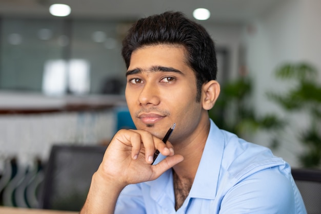 Portrait of young Indian businessman or student sitting with pen