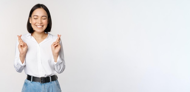 Free Photo portrait of young korean woman asian girl cross fingers and praying making wish anticipating waiting for results standing over white background