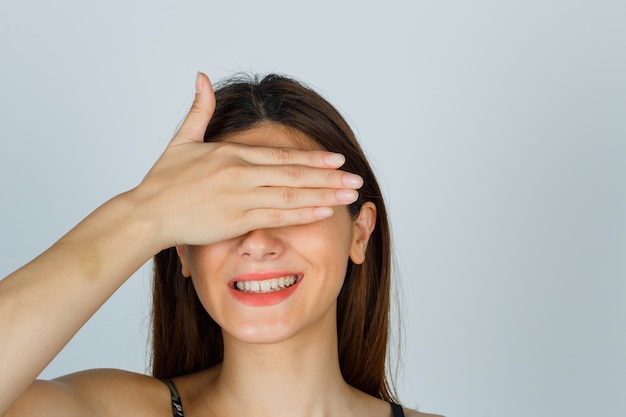 Free photo portrait of young lady holding hand on eyes in top and looking cheerful front view