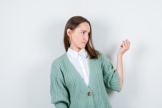 Portrait of young lady inviting to come while looking aside in shirt, cardigan and looking focused front view