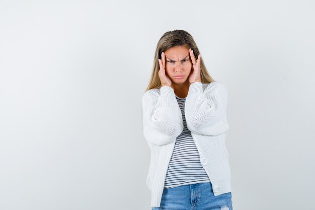 Portrait of young lady pulling skin on her forehead in t-shirt, jacket and looking gloomy front view