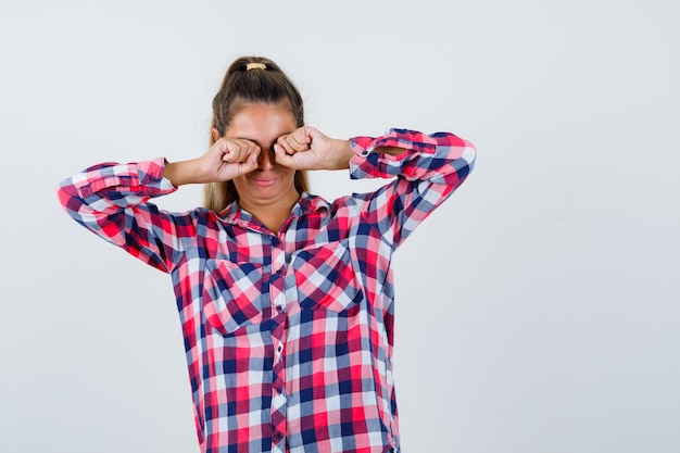 Free Photo portrait of young lady rubbing eyes while crying in checked shirt and looking offended front view