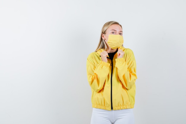 Free Photo portrait of young lady showing winner gesture in jacket, pants, mask and looking lucky front view