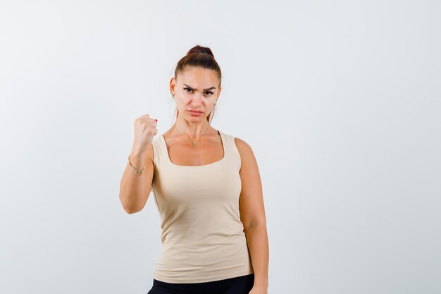 Portrait of young lady showing winner gesture in tank top and looking serious front view