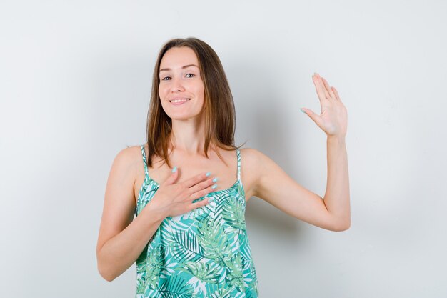 Portrait of young lady waving hand for greeting in blouse and looking cheery front view