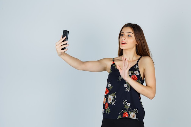 Portrait of young lady waving hand on video call in blouse and looking glad front view