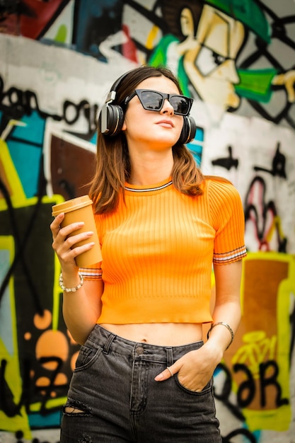 Portrait of young lady wearing headphones and holding coffee cup