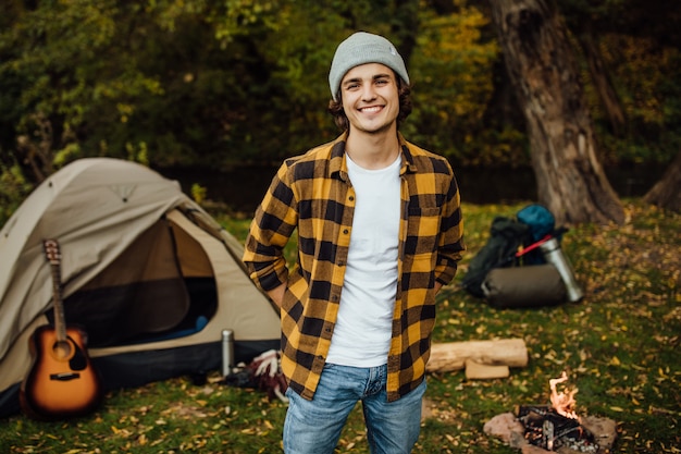 Portrait of young male tourist standing in the forest with tent