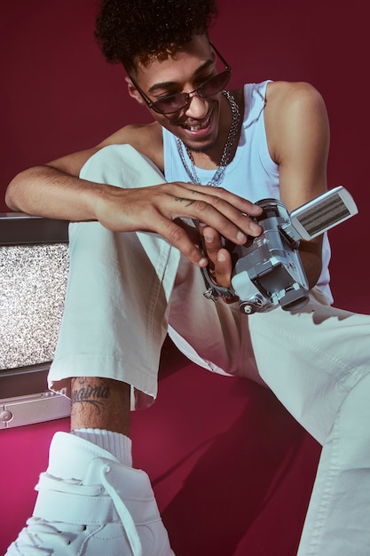 Free photo portrait of young man in 2000s fashion style posing with camera and sunglasses