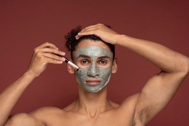 Portrait of a young man applying face mask on his face with a make-up brush