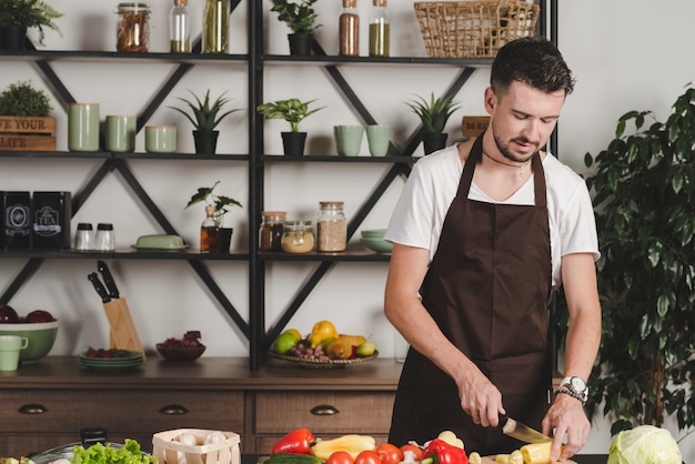 Portrait of young man cutting vegetables with knife in the kitchen