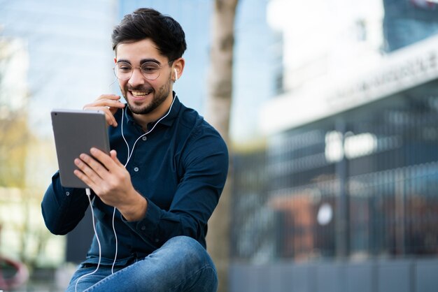 Portrait of young man having a video call on digital tablet while standing outdoors