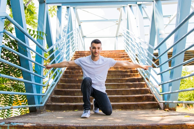 Portrait of a young man kneeling on stairs stretching his arms