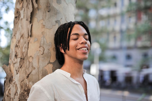 Free photo portrait of a young man leaning against a tree