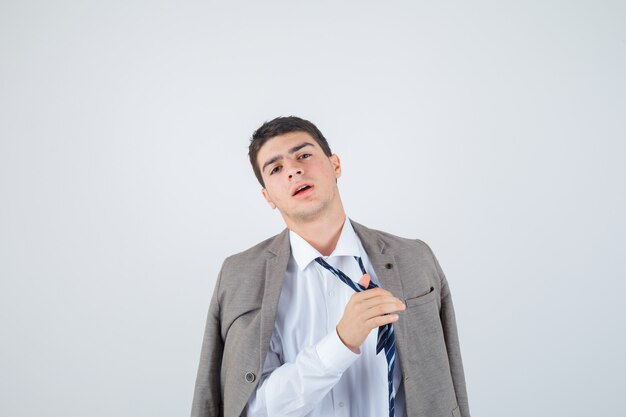 Portrait of young man loosen tie while posing in shirt, jacket, striped tie and looking fatigued