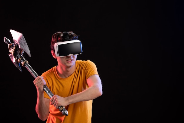 Free photo portrait of young man playing vr with battle axe on dark wall