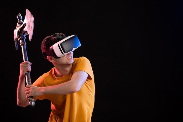 Portrait of young man playing vr with battle axe on dark wall