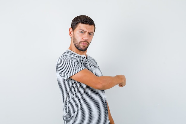 Portrait of young man pointing back in t-shirt and looking hesitative front view