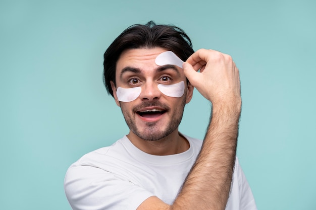 Portrait of a young man removing the under-eye patches from his forehead