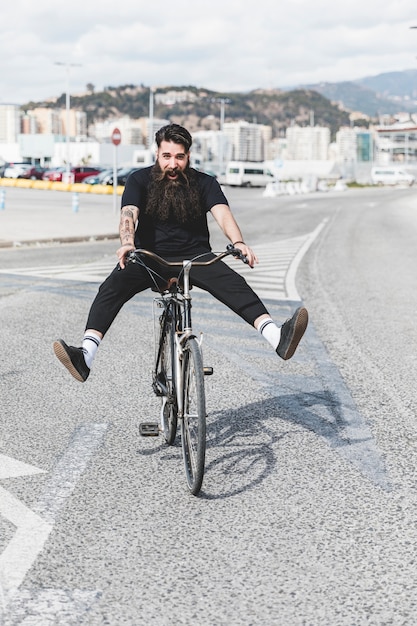 Free photo portrait of young man riding bicycle on road with legs kicked out