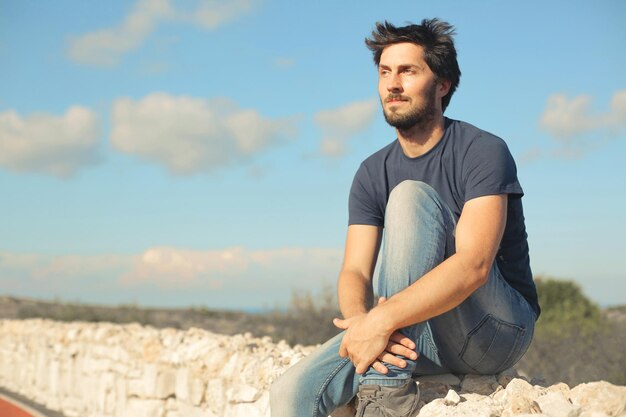 portrait of young man sitting on a low wall