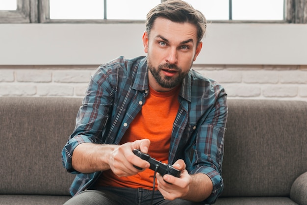 Portrait of a young man sitting on sofa playing the video game