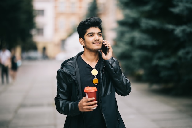 Portrait of young man talking on phone and walking on the street